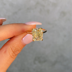Yellow diamond ring with gold setting on a white background held by female