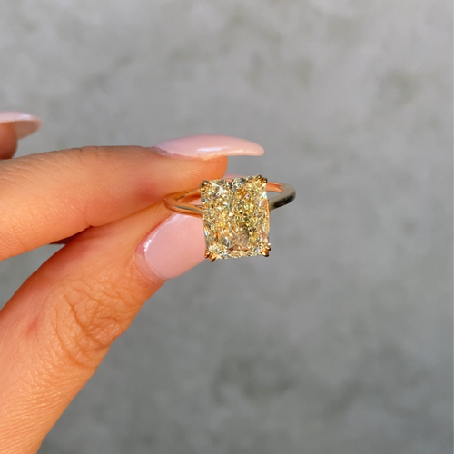 Yellow diamond ring with gold setting on a white background held by female 