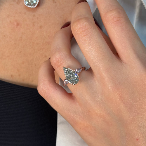 Hand wearing a green diamond ring with a blurred background