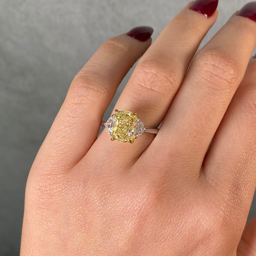 Hand wearing an elongated radiant cut yellow diamond ring against a neutral background