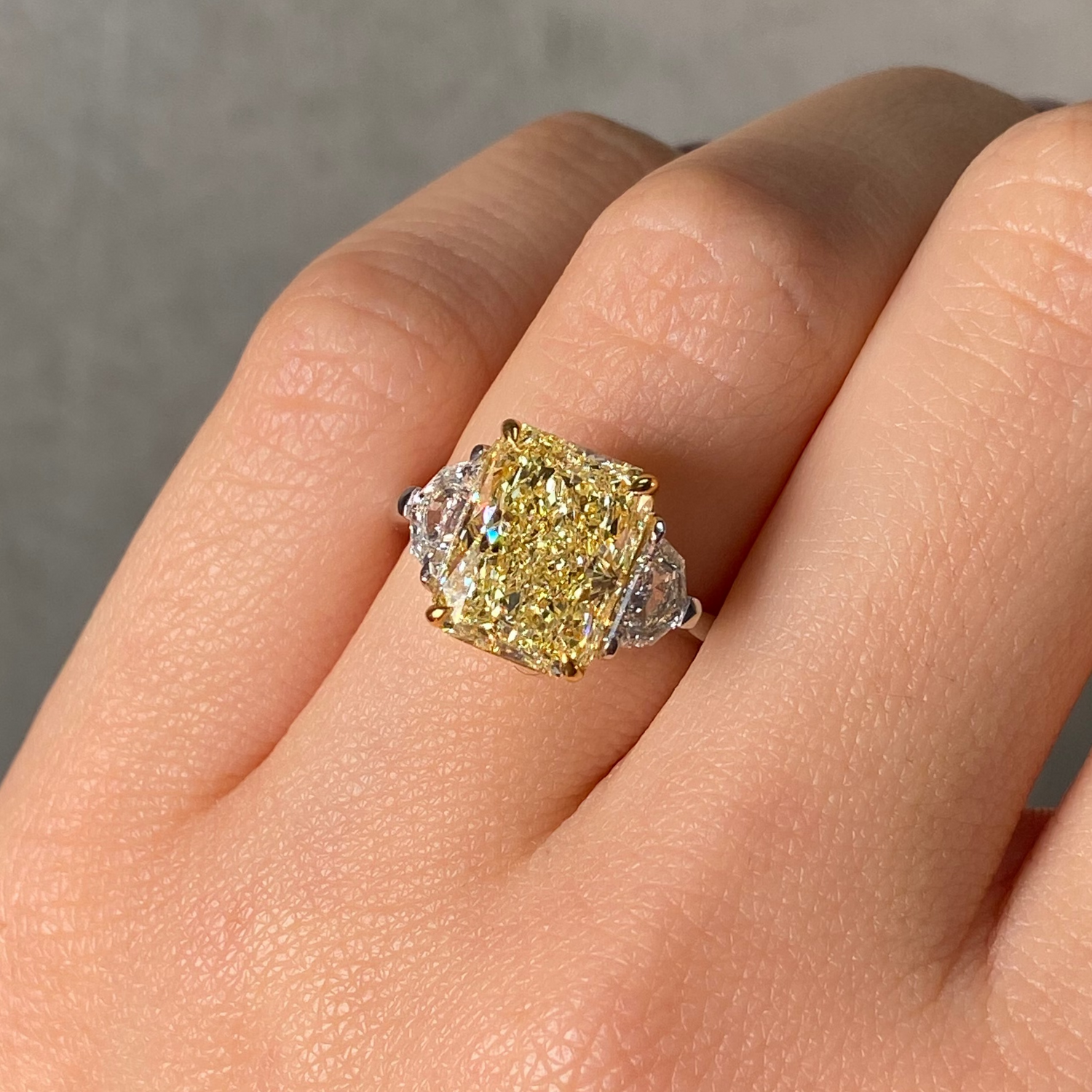  Gold ring with a large yellow diamond on a hand against a neutral background