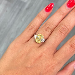 Unique Three-stone ring featuring a GIA-certified fancy yellow elongated cushion diamond with VVS2 clarity.