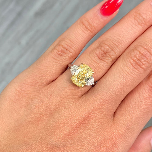 Unique Three-stone ring featuring a GIA-certified fancy yellow elongated cushion diamond with VVS2 clarity.