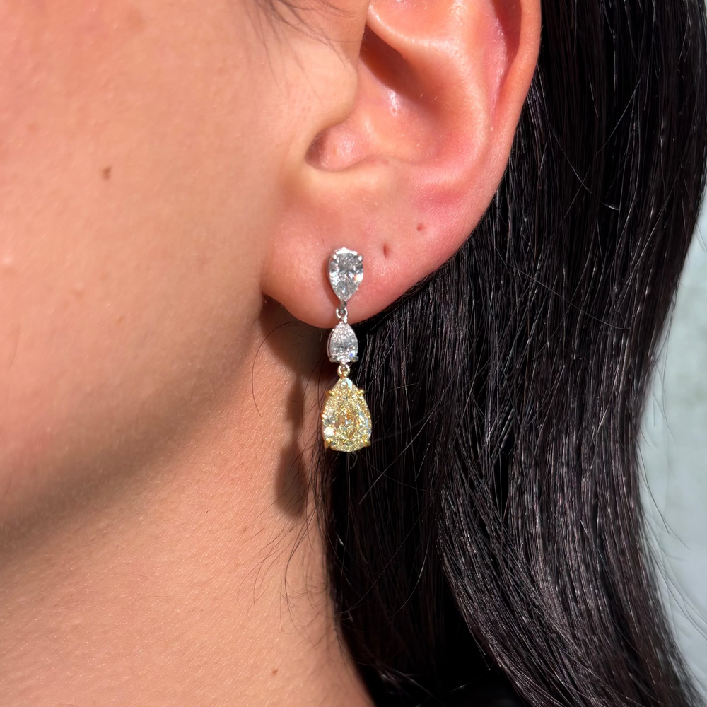 Close-up of an ear wearing a diamond earring with a yellow diamond