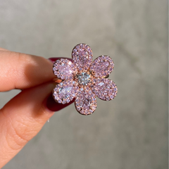 Pink flower-shaped ring held by a hand against a neutral background