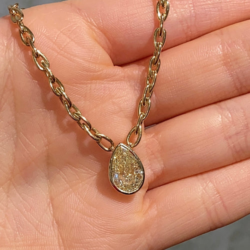 Gold necklace with a teardrop-shaped pendant held in a hand against a gray background