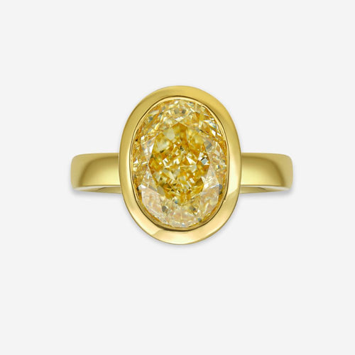 Gold bezel ring with a yellow diamond on a white background