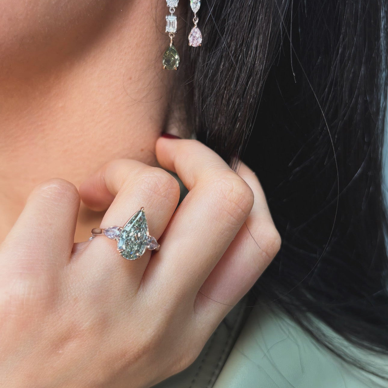 Ring with a green pear-shaped diamond and pink diamond side stones on a female hand 