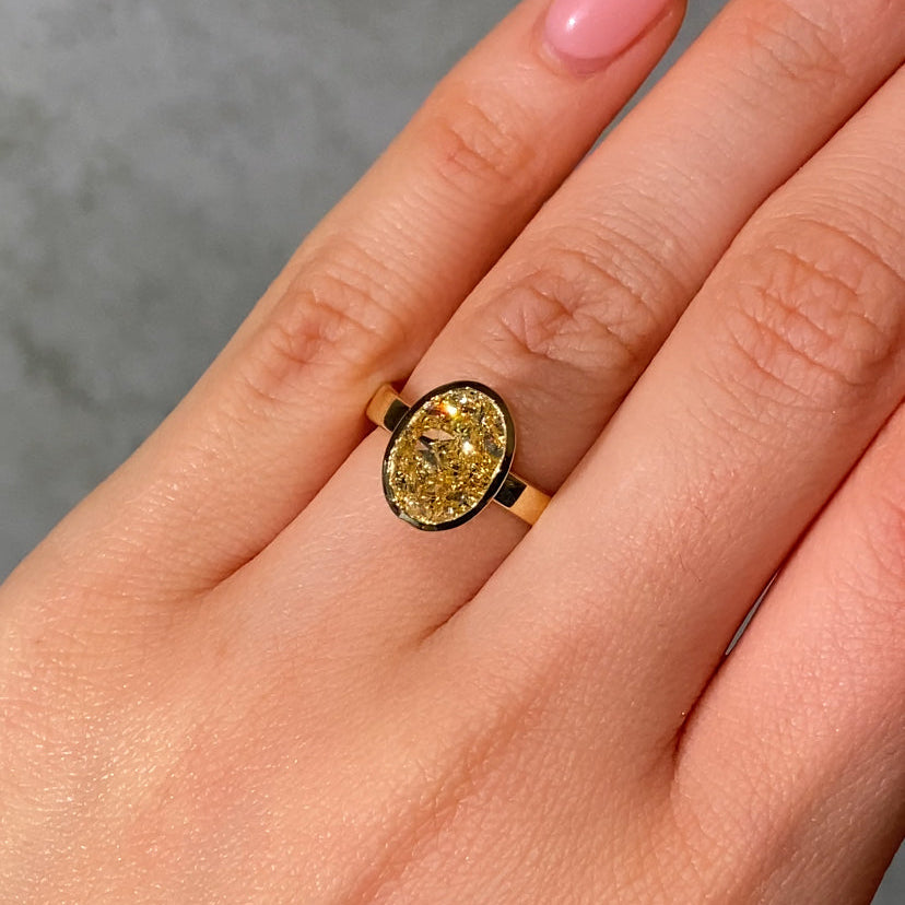 yellow diamond gold bezel ring balck background on female hand 