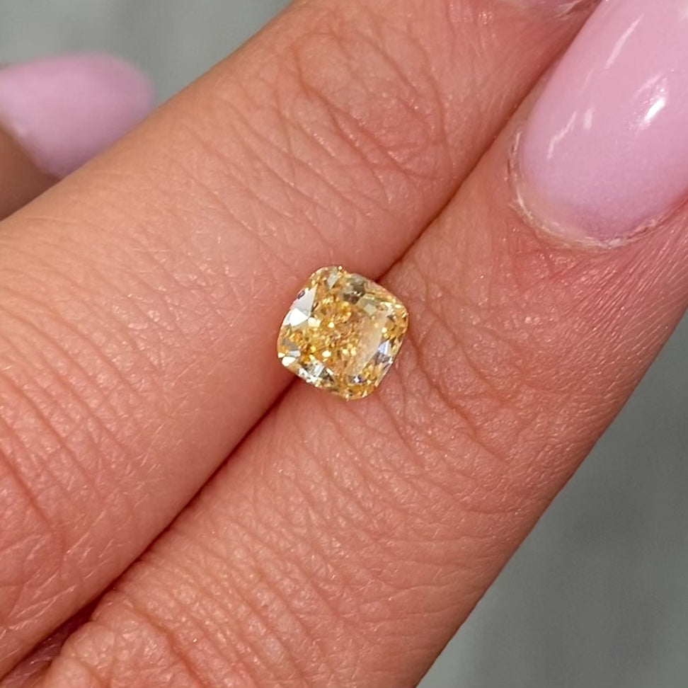 Vivid yellow-orange cushion-cut diamond with intricate facets, reflecting light on a soft background.
