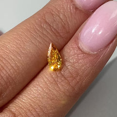 Vivid orange-yellow pear-shaped diamond with a brilliant cut, showcased on a soft, light background.